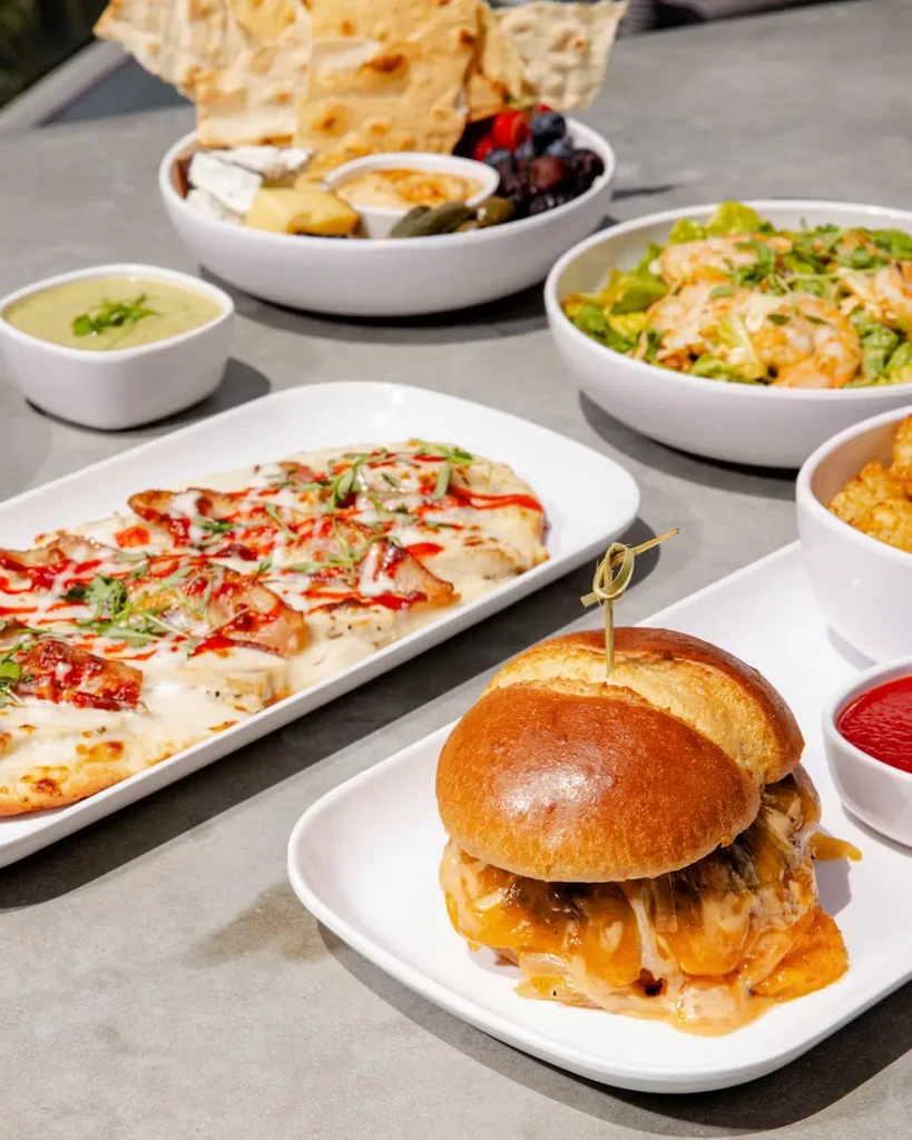 Table with a gourmet burger, flatbread, charcuterie, salad, and appetizers.