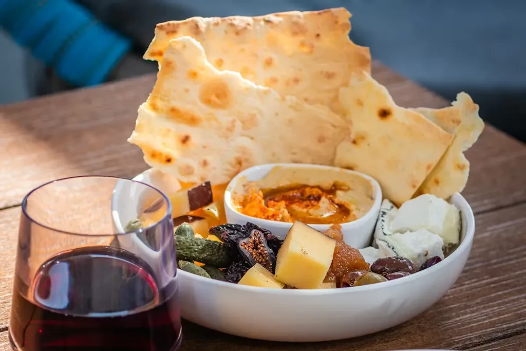 Bowl with flatbread, cheese, dip, olives, figs; glass of red wine.
