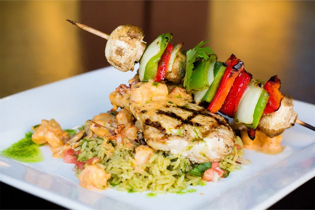 Grilled fish or chicken, orange sauce, green rice, and vegetable skewer.