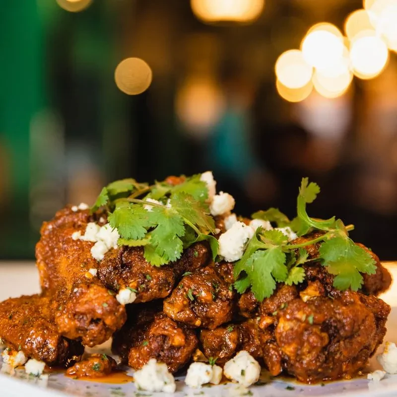Plate of chicken wings with reddish-brown sauce, cilantro, and crumbled cheese.