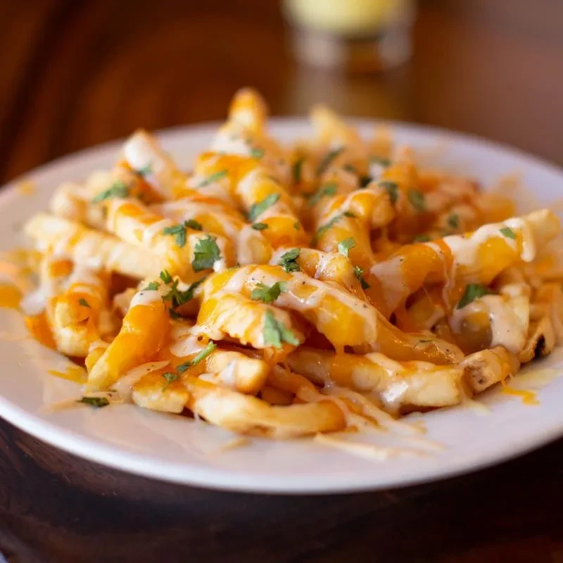 Loaded golden french fries with melted cheese, creamy sauce, and green herbs.