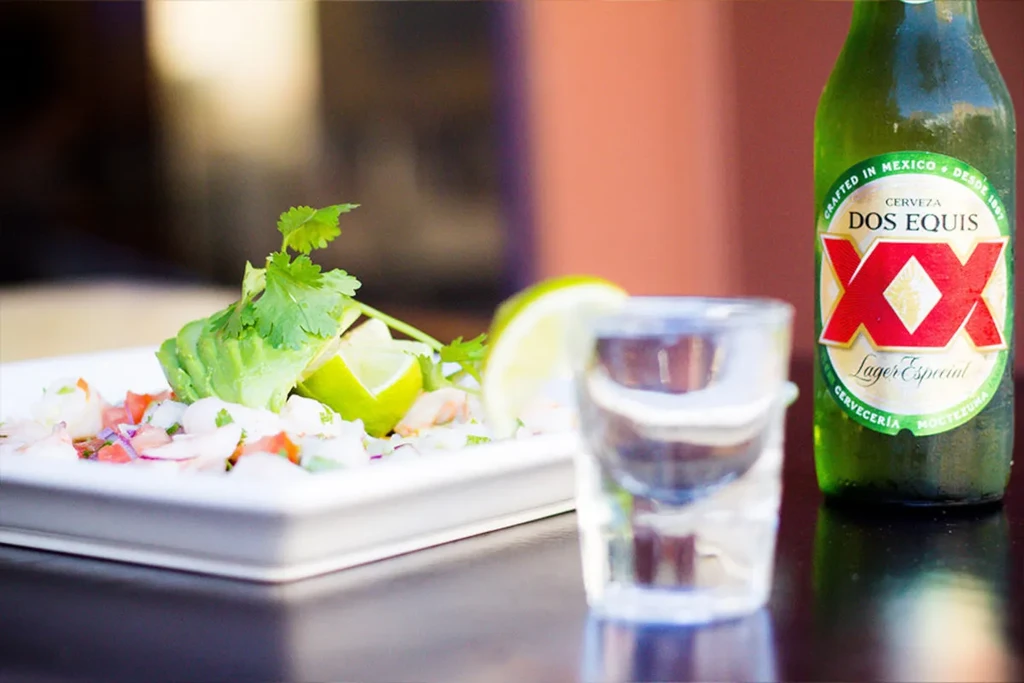 Close-up of ceviche, avocado, lime, and Dos Equis XX beer.