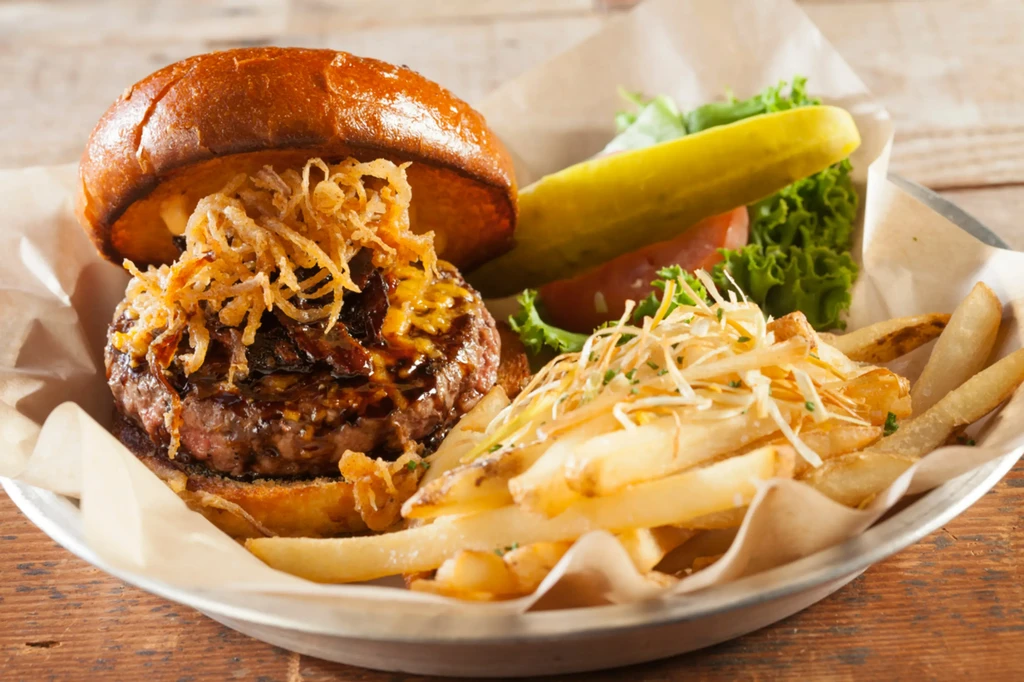 Juicy burger with cheese, bacon, onions, fries, salad, and pickle.