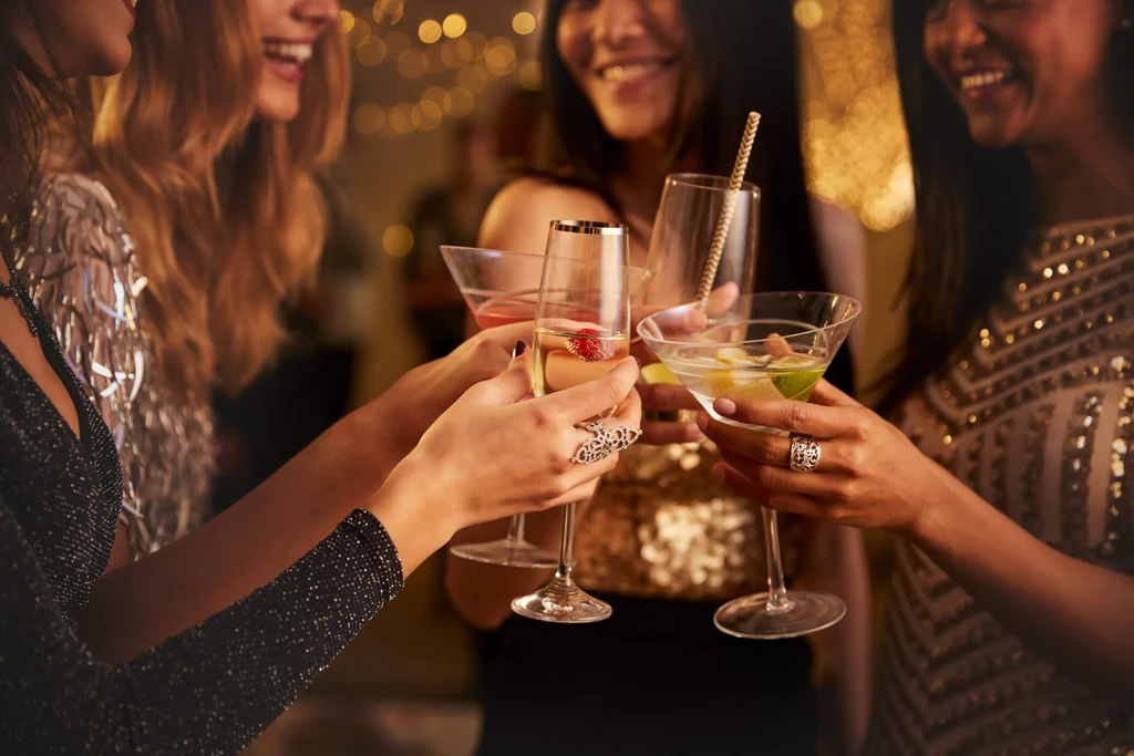 Four elegantly dressed women's hands toasting with various cocktails.