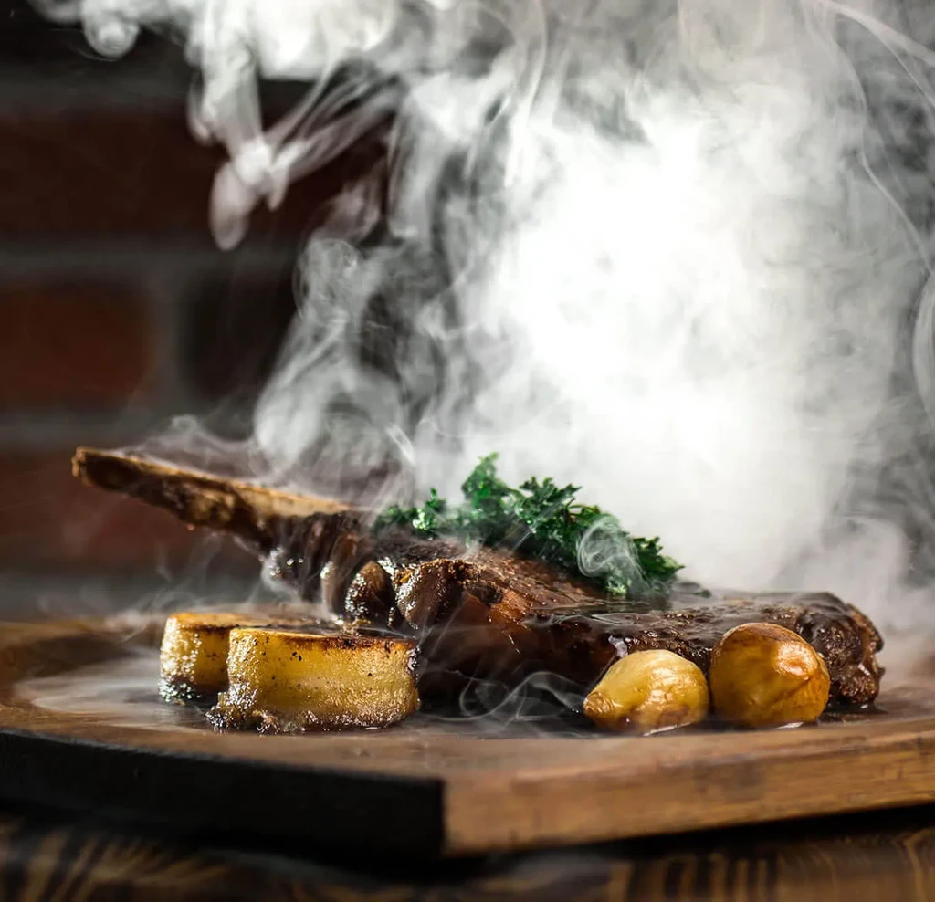 A tomahawk steak, potatoes, and herbs enveloped in smoke.