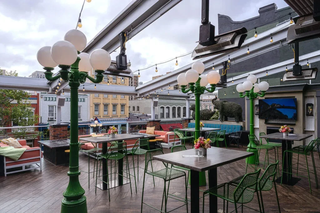 Rooftop patio with green bar stools, orange sofas, and decorative lamps.