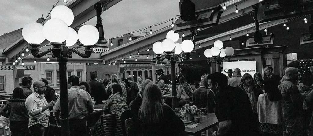 Lively black and white outdoor event with festive lights and "Incentive" screen.