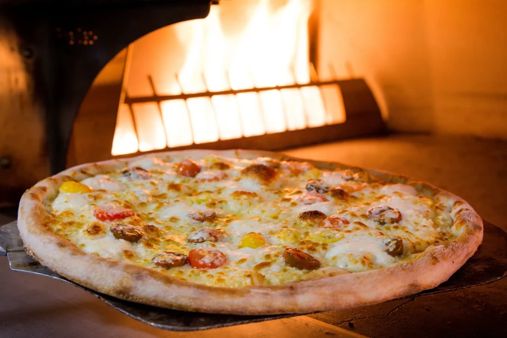 Pizza with colorful tomatoes on a peel inside wood-fired oven.