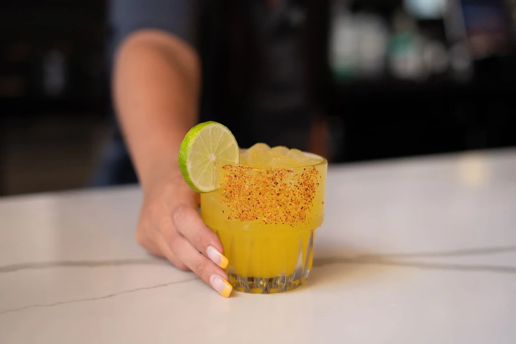 Yellow frozen cocktail with spiced rim and lime, held by hand.