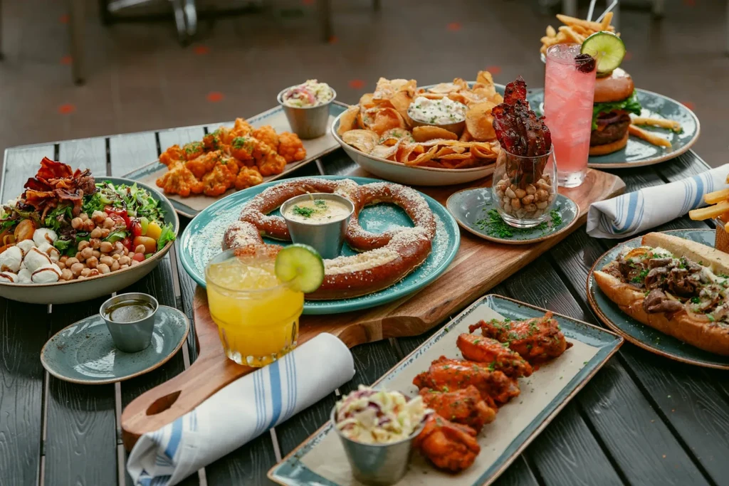 A wooden table laden with various casual dishes and colorful cocktails.