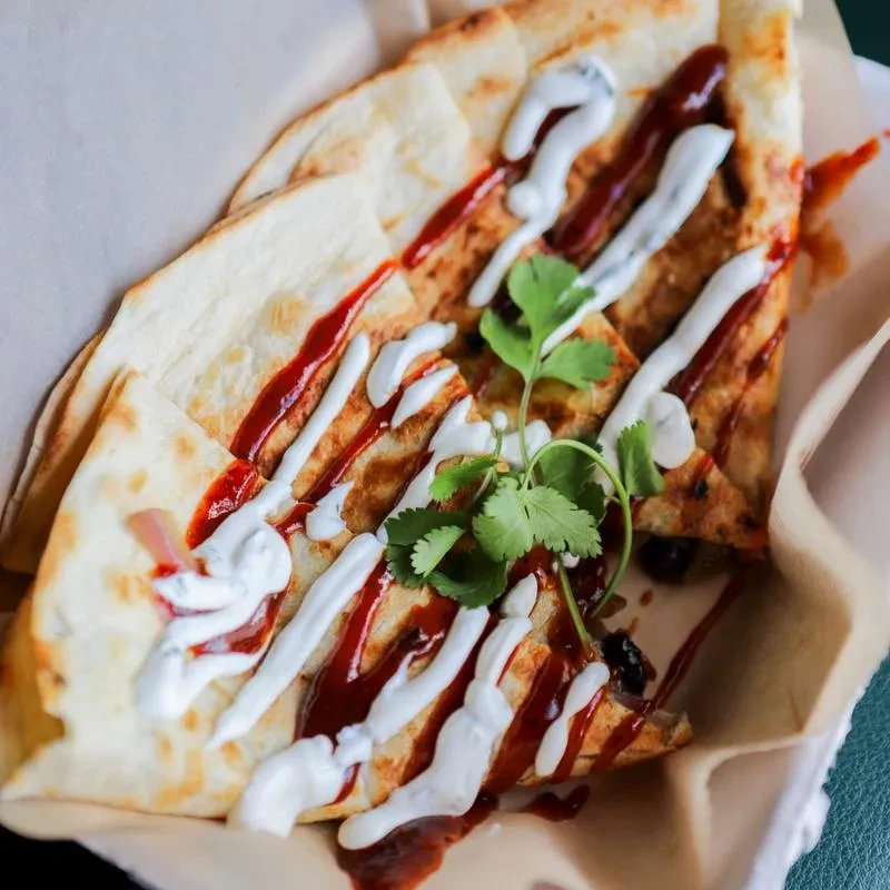 Quesadilla triangles with two sauces and cilantro in a paper container.