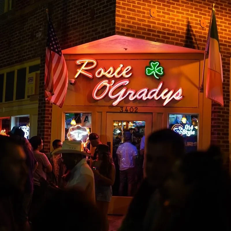 Lively Rosie O'Gradys bar exterior with neon sign and flags at night.