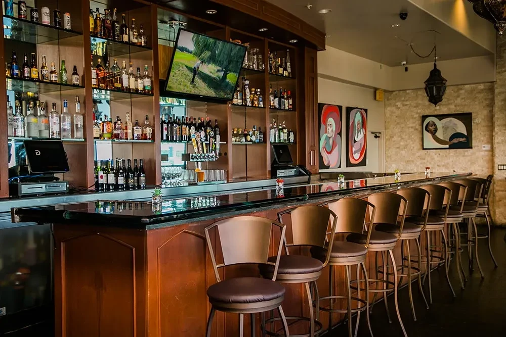 Empty bar area with stocked bottles, bronze stools, and golf on TV.