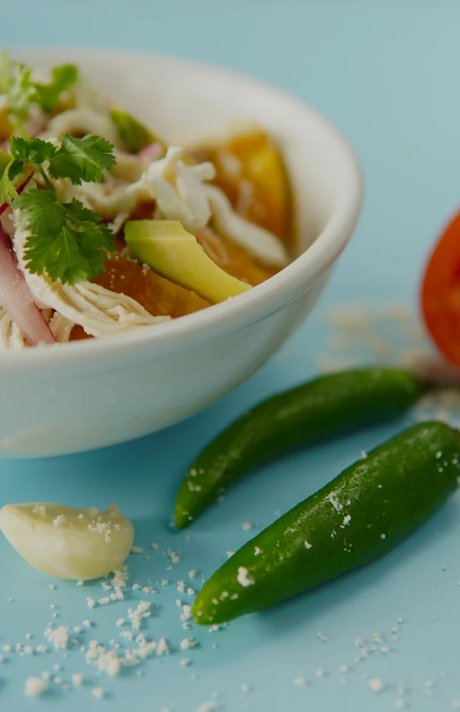 Colorful bowl of chicken and avocado soup with chilis and garlic.