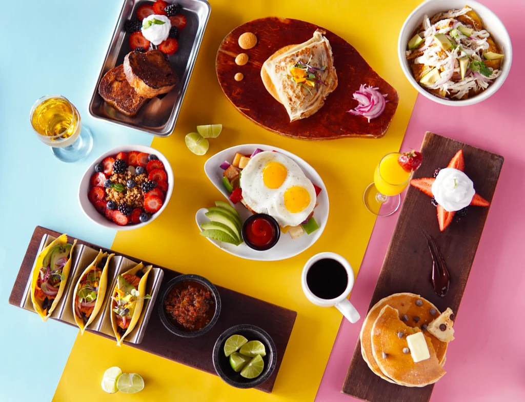 Vibrant flat-lay of numerous breakfast and brunch dishes on colored blocks.