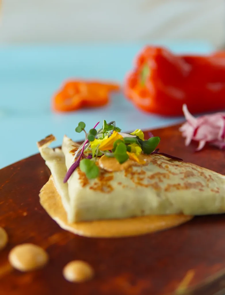 Artfully plated triangular food, orange sauce, microgreens, and yellow flowers.