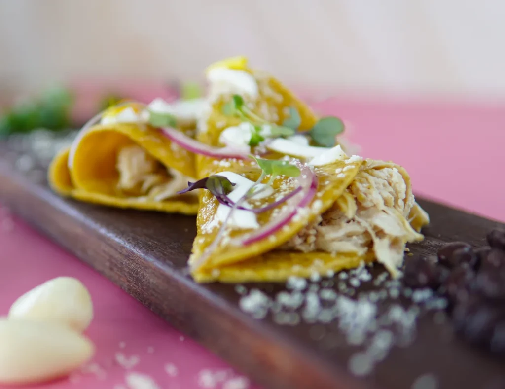 Rolled chicken tortillas with cream and herbs on wood, pink background.