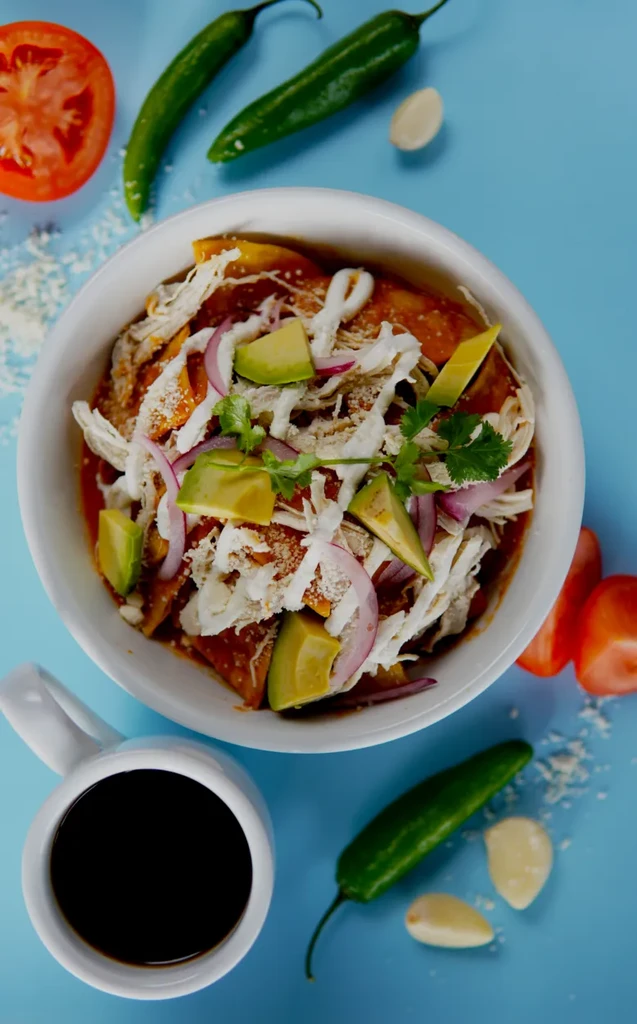 Overhead: Mexican dish with chicken, avocado, cilantro, coffee on blue.