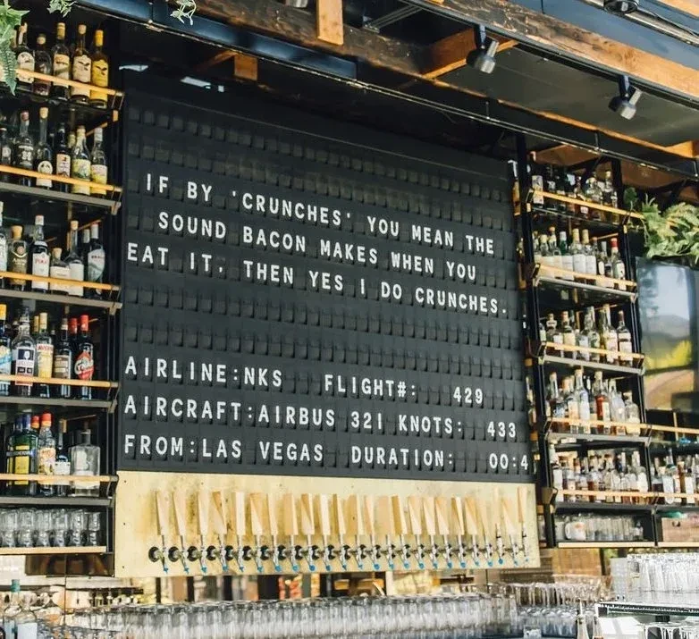 Bar interior: letter board with humorous quote, flight data, and beer taps.