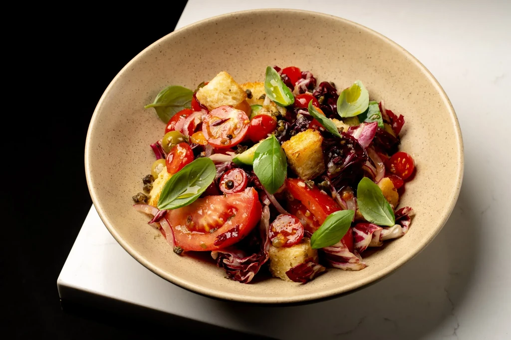 Colorful salad with tomatoes, croutons, basil, radicchio, olives in bowl.