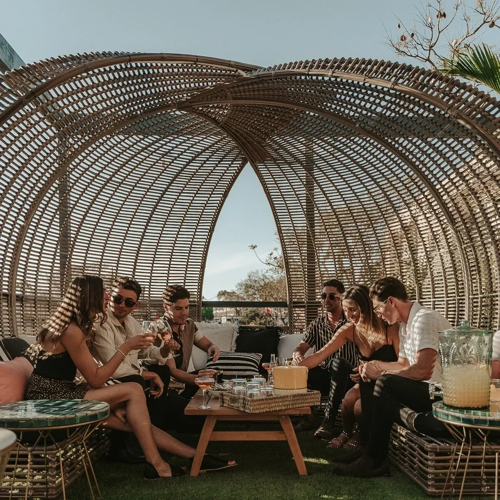 Six people enjoy drinks and food in a woven outdoor dome.