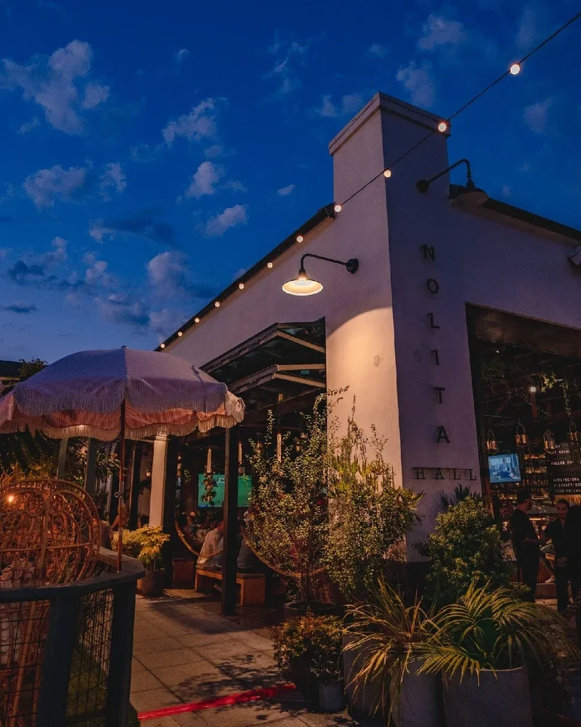 Nolita Hall exterior at dusk, illuminated patio with indistinct people.