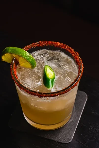 Margarita in rocks glass, chili-salted rim, lime wedge, jalapeño slice.