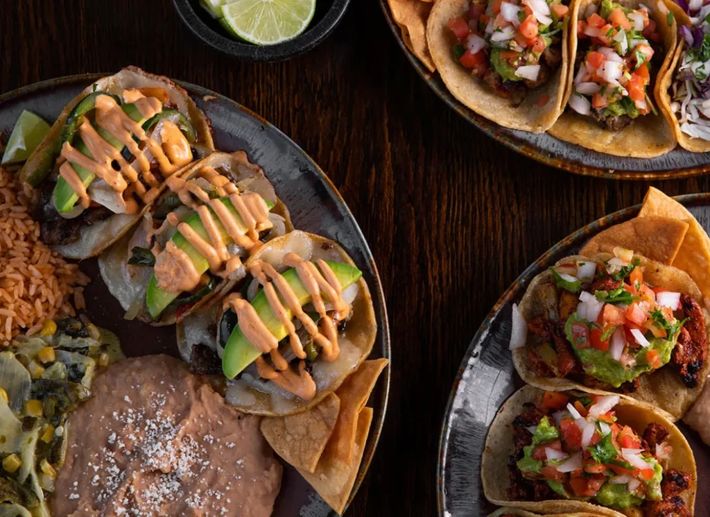 High-angle view of multiple plates of Mexican tacos and sides.