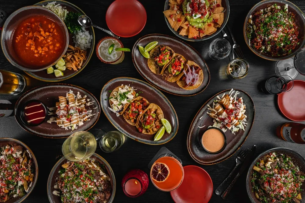Flat lay of Mexican tacos, nachos, pozole, and various drinks.