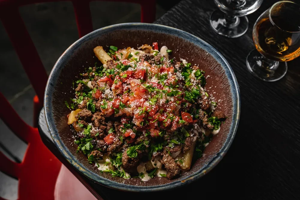 Close-up of loaded fries with meat, cheese, salsa, and fresh herbs.