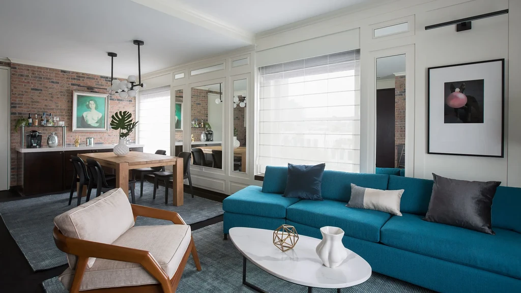 Modern living-dining room with a teal sofa, dining table, and brick bar.