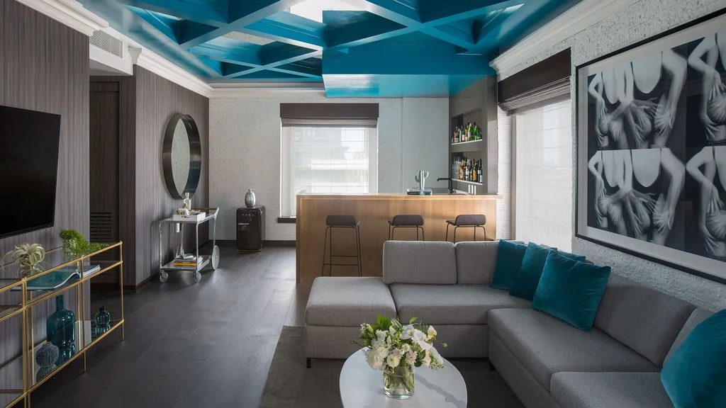 Contemporary interior with blue geometric ceiling, grey sofa, bar, and abstract art.