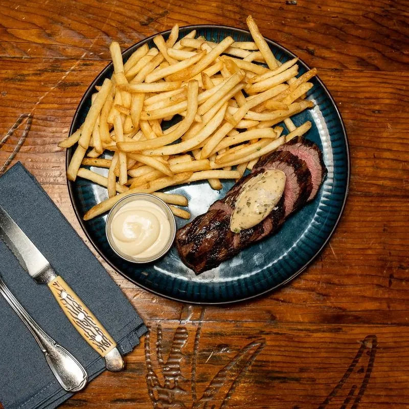 Plate of grilled medium-rare steak, creamy sauce, and french fries.