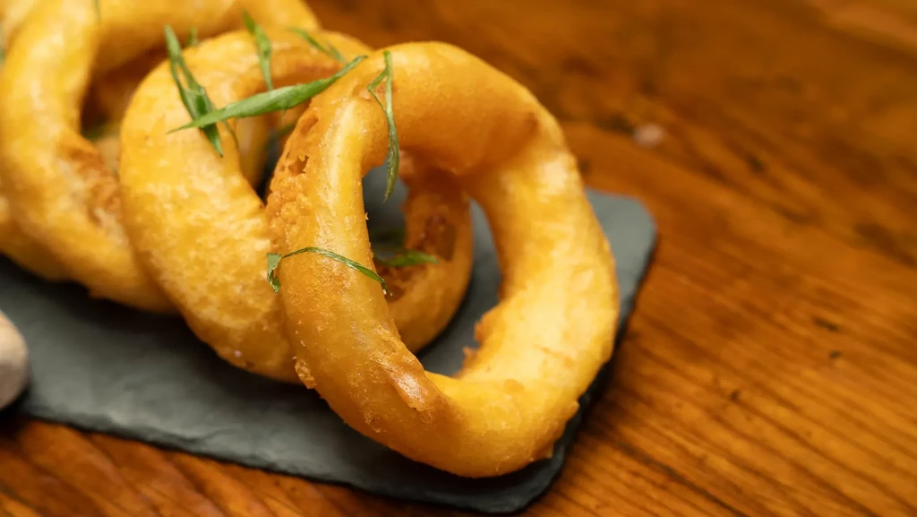 Crispy golden-brown fried rings with herb garnish on a slate.