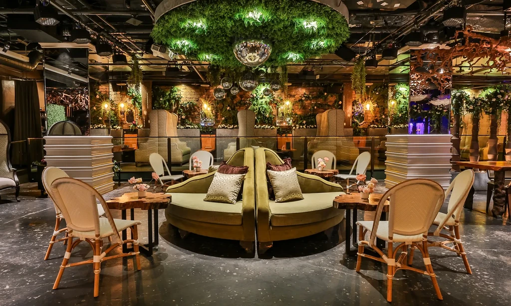 Upscale lounge: green velvet sofa, garden decor, suspended disco balls.