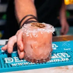 Pink cocktail with coconut rim and citrus slice on a blue bar mat.