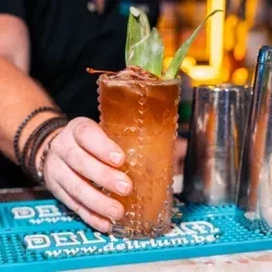 Hand holding an amber cocktail garnished with a frond and cherry.