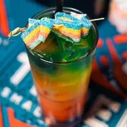 Layered green, orange, red drink with rainbow sour candy strips.