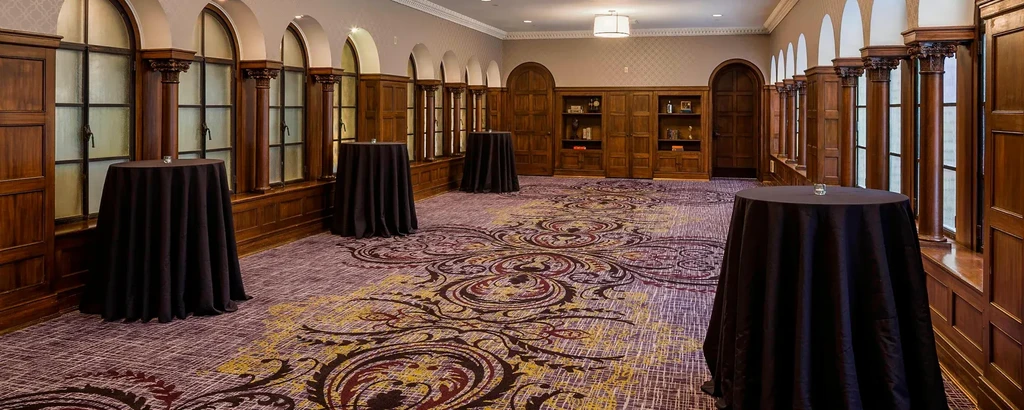 Elegant, empty event room with dark wood, patterned carpet, draped tables.