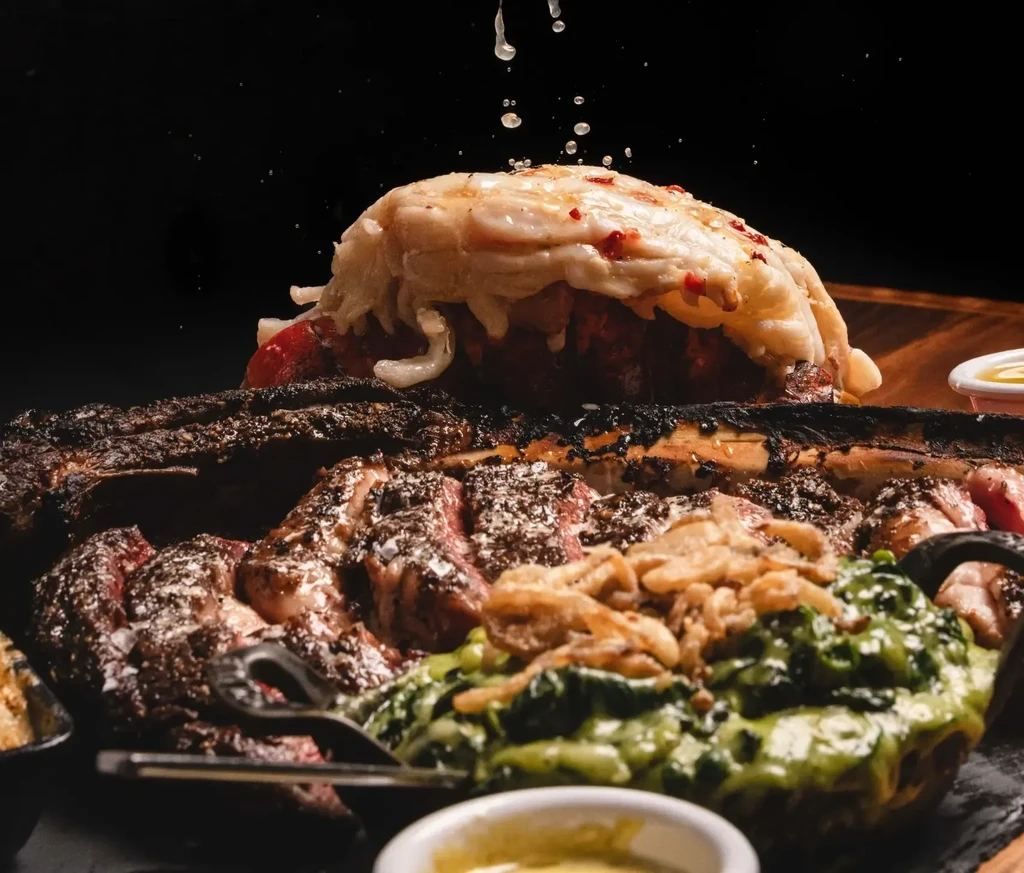 Grilled meat, lobster, melted cheese, drizzled sauce, and green side dish.