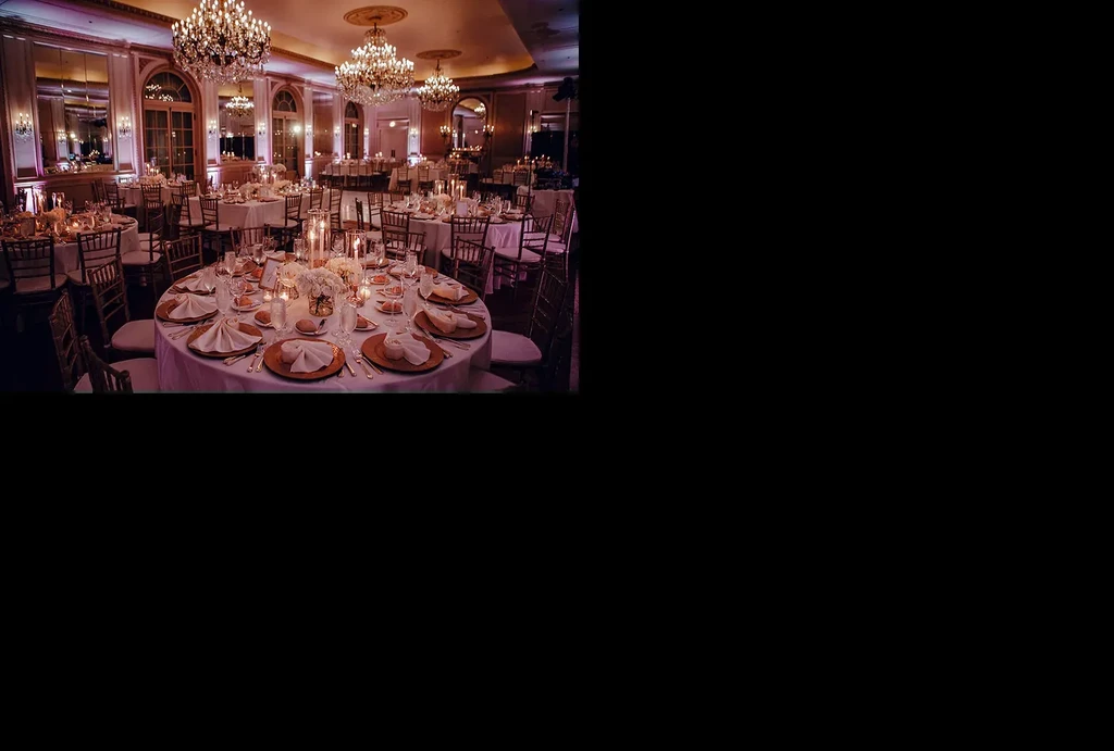 Elegant banquet hall with round tables, flowers, glowing candles, and chandeliers.