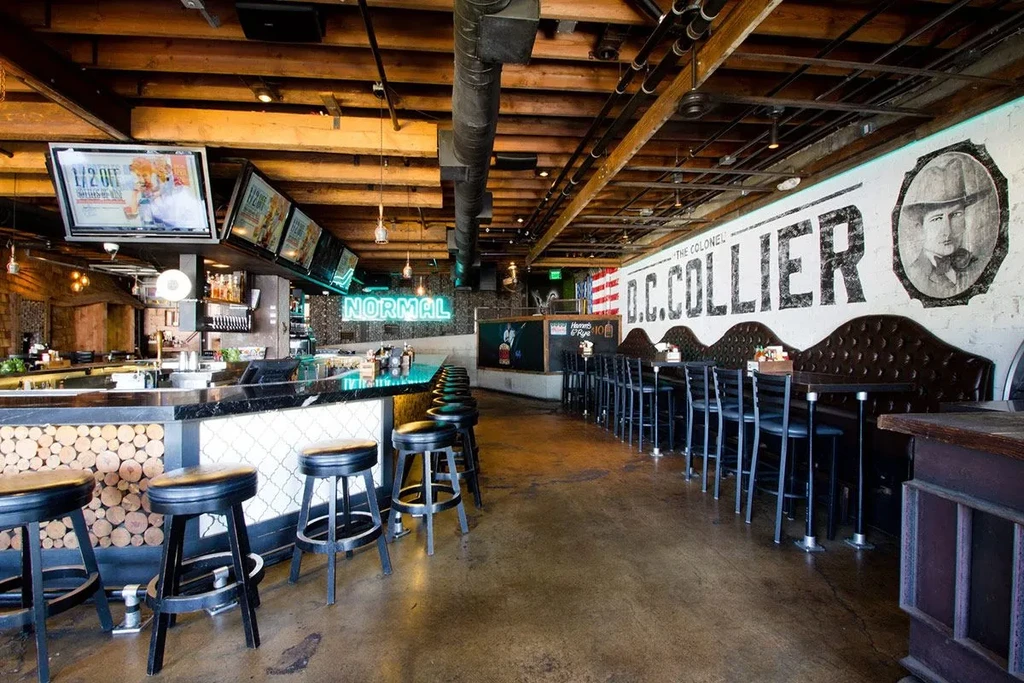 Industrial-chic bar with log-slice stools, NORMAL neon, and Colonel mural.