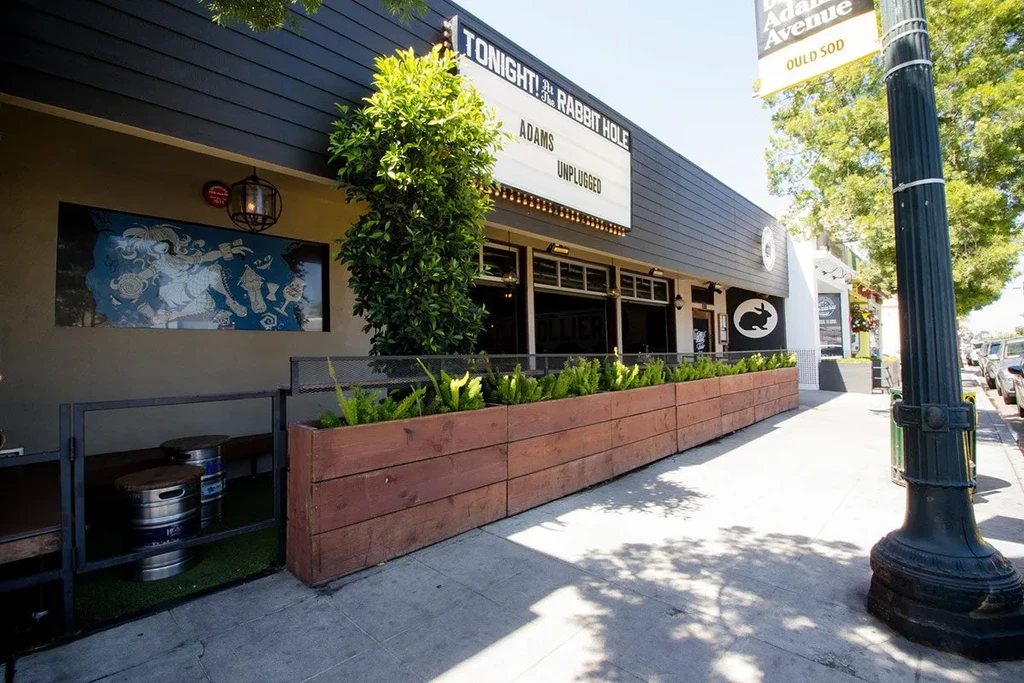 Exterior of "The Rabbit Hole" restaurant with marquee sign, patio, and mural.