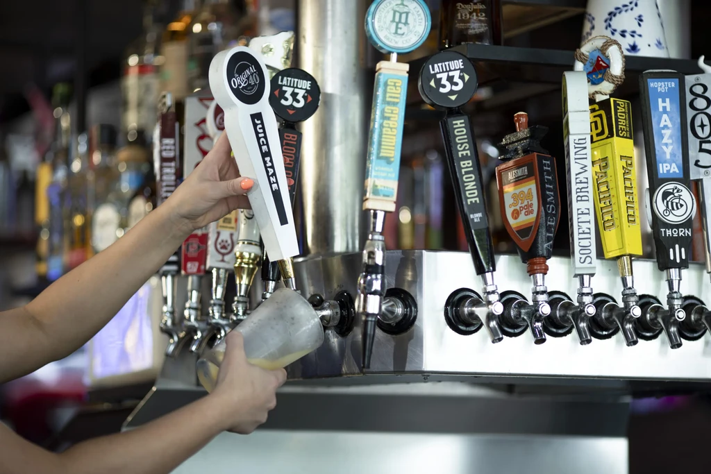 Hands pour beer into a frosted glass from a tap, many branded taps.