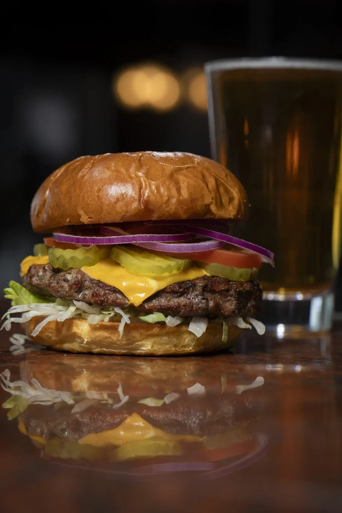 A gourmet cheeseburger with melted cheese, fresh toppings, and a beer.