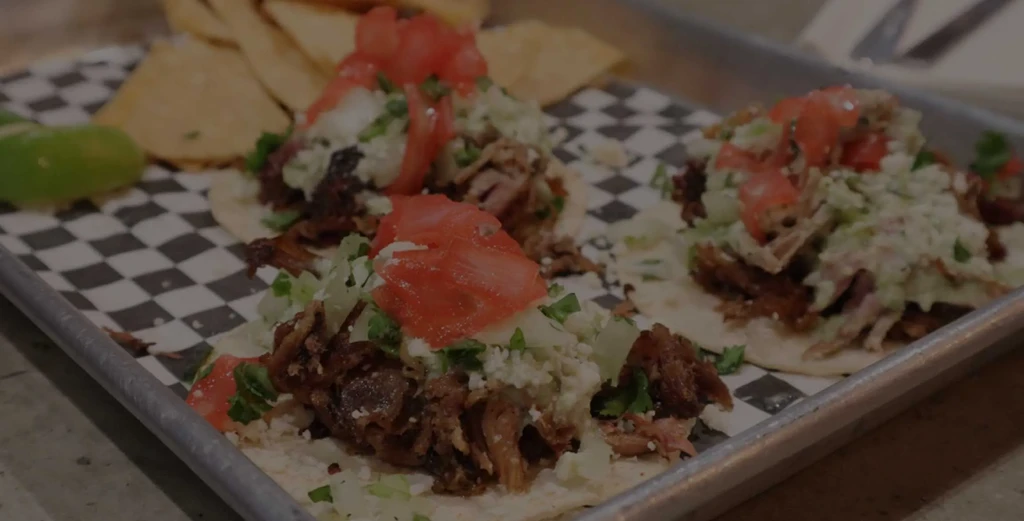 Three shredded meat tacos with toppings, lime, and chips on a tray.