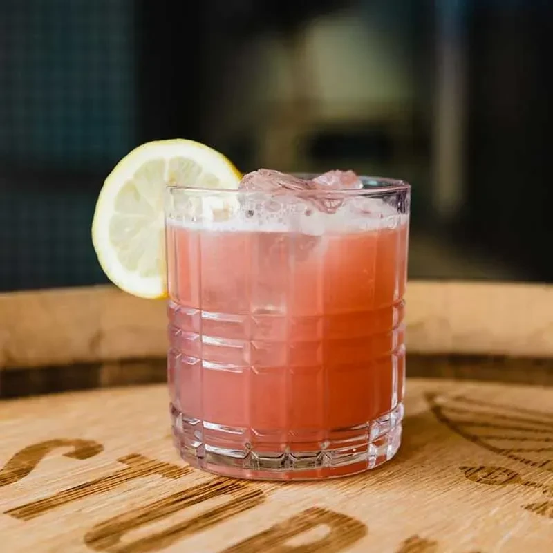 Rosy pink cocktail in textured glass with lemon slice on wood.