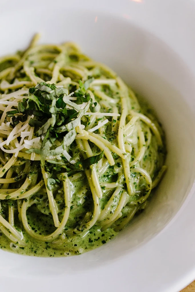 Pasta with creamy green sauce, shredded cheese, and fresh basil.