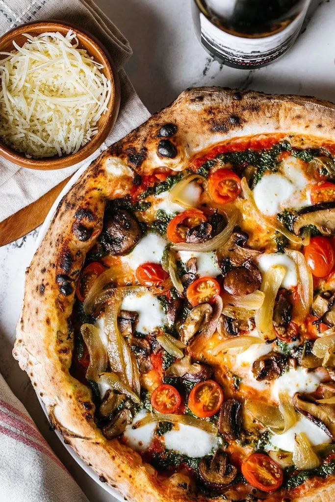 Neapolitan pizza with pesto, mozzarella, tomatoes, mushrooms, and onions.