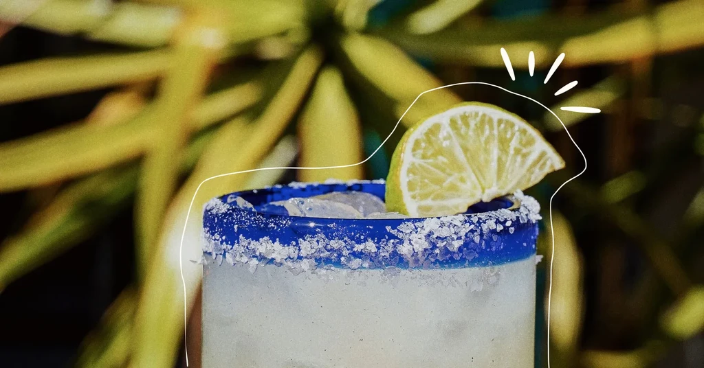 Frosty margarita with a salted blue rim and lime outdoors.